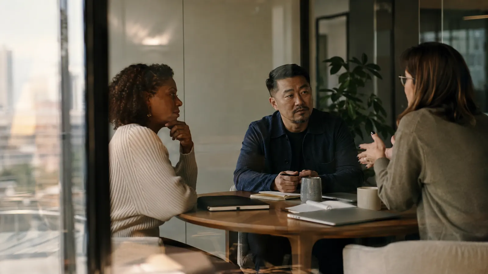 Three sales colleagues rehearse a procurement negotiation around a table in a warm, quiet meeting room.